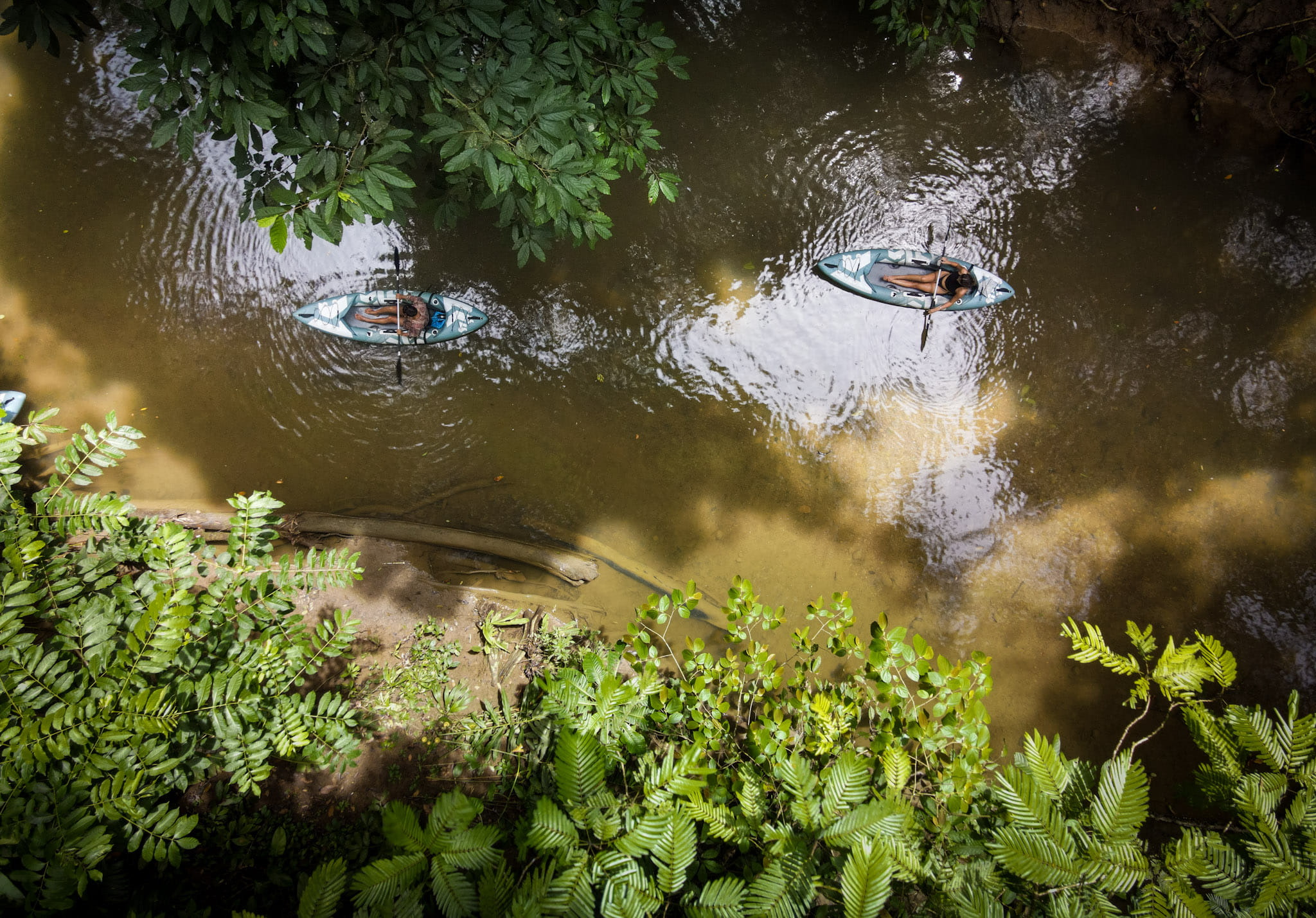 Drone view of two people paddling kayaks along a calm tropical river surrounded by dense green rainforest in Punta Uva, Costa Rica.