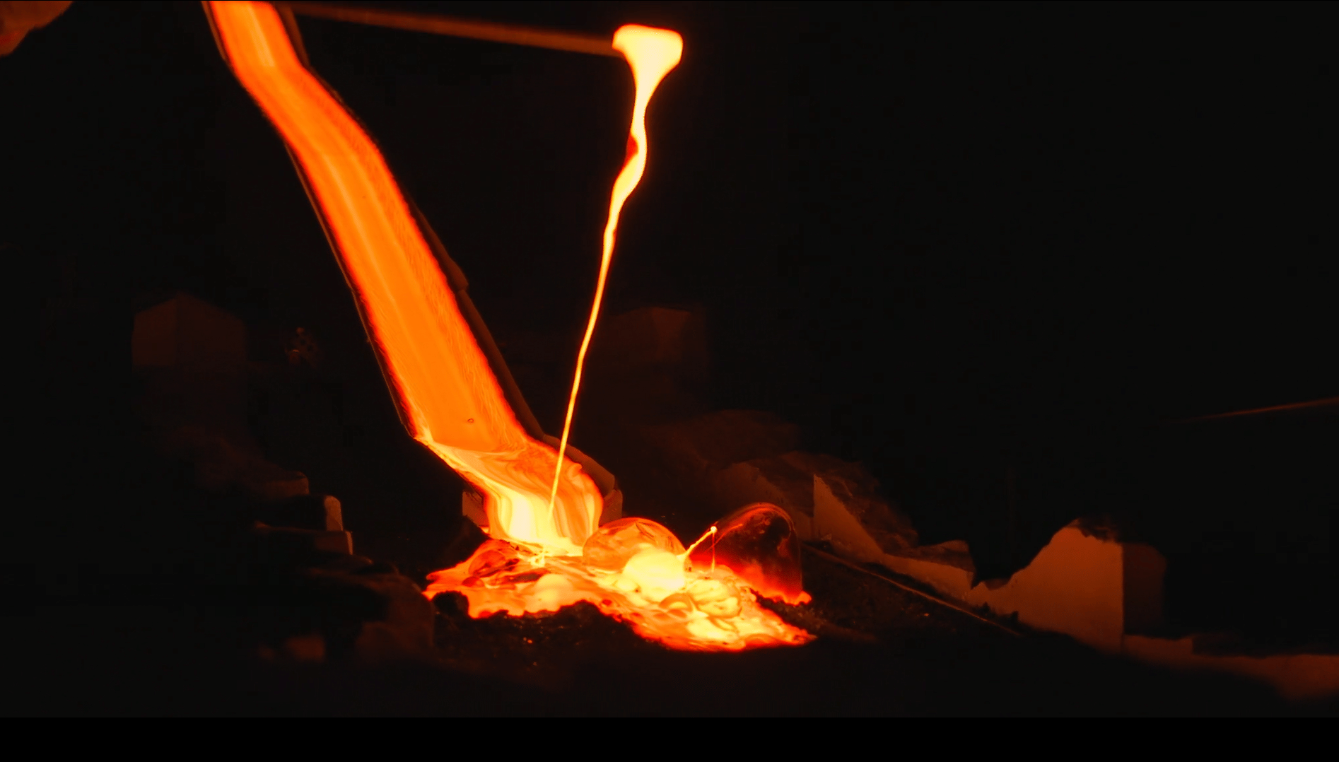 Molten lava flows in bright orange from a tilted container into a cooling pit, glowing intensely against a dark background.