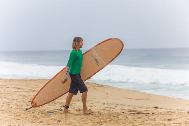 Surfer carrying a longboard on the beach in Los Cabos before surfing