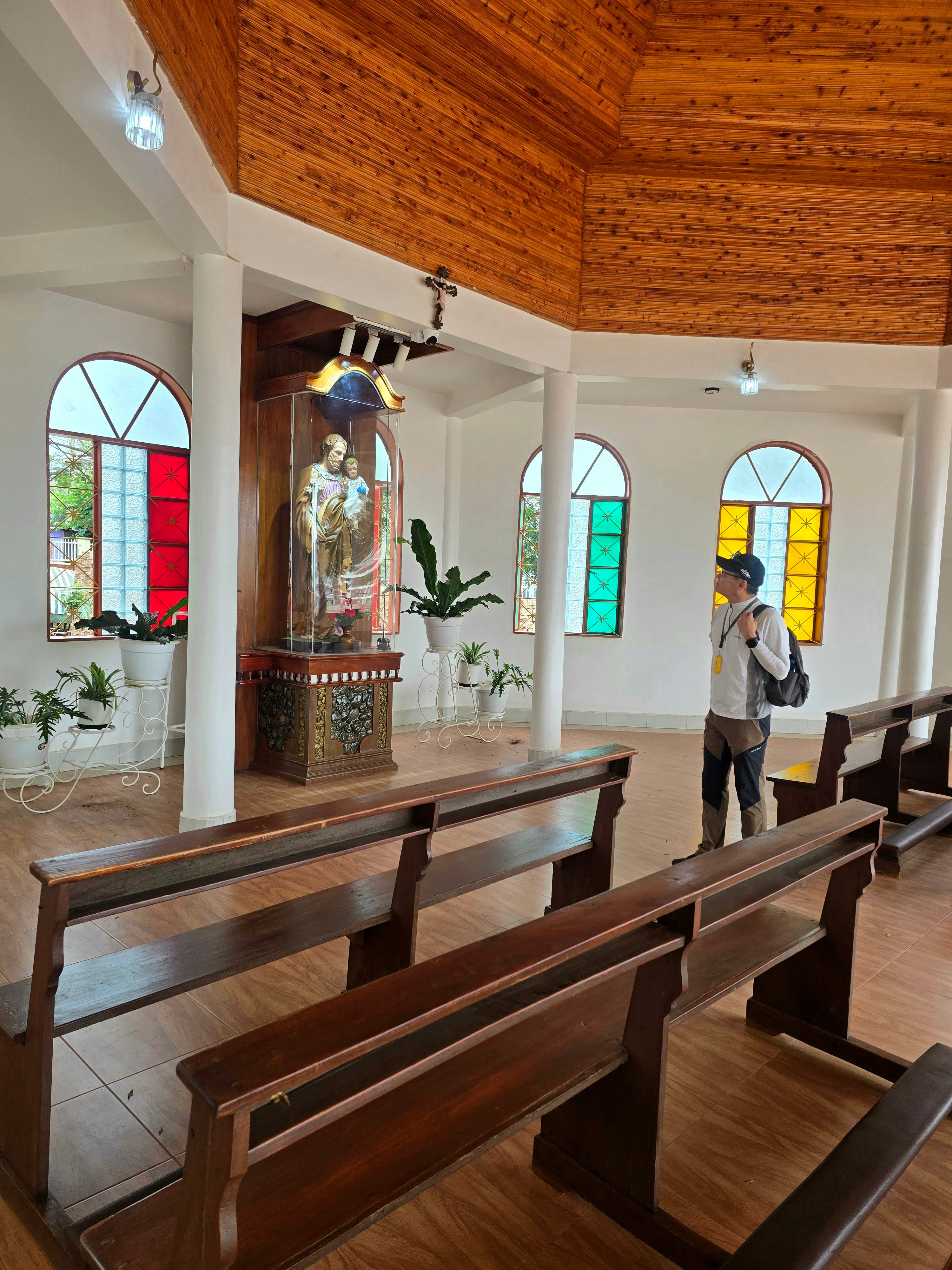 Interior view of a church sanctuary featuring colorful stained glass windows, wooden pews, and natural light.