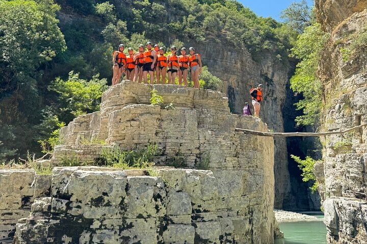 A group of people standing at the edge of a cliff , preparing to jump into the water .