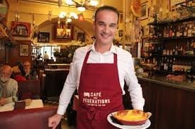 A friendly waiter in a traditional bouchon lyonnais, wearing a red apron and serving a freshly prepared dish in a cozy restaurant setting.