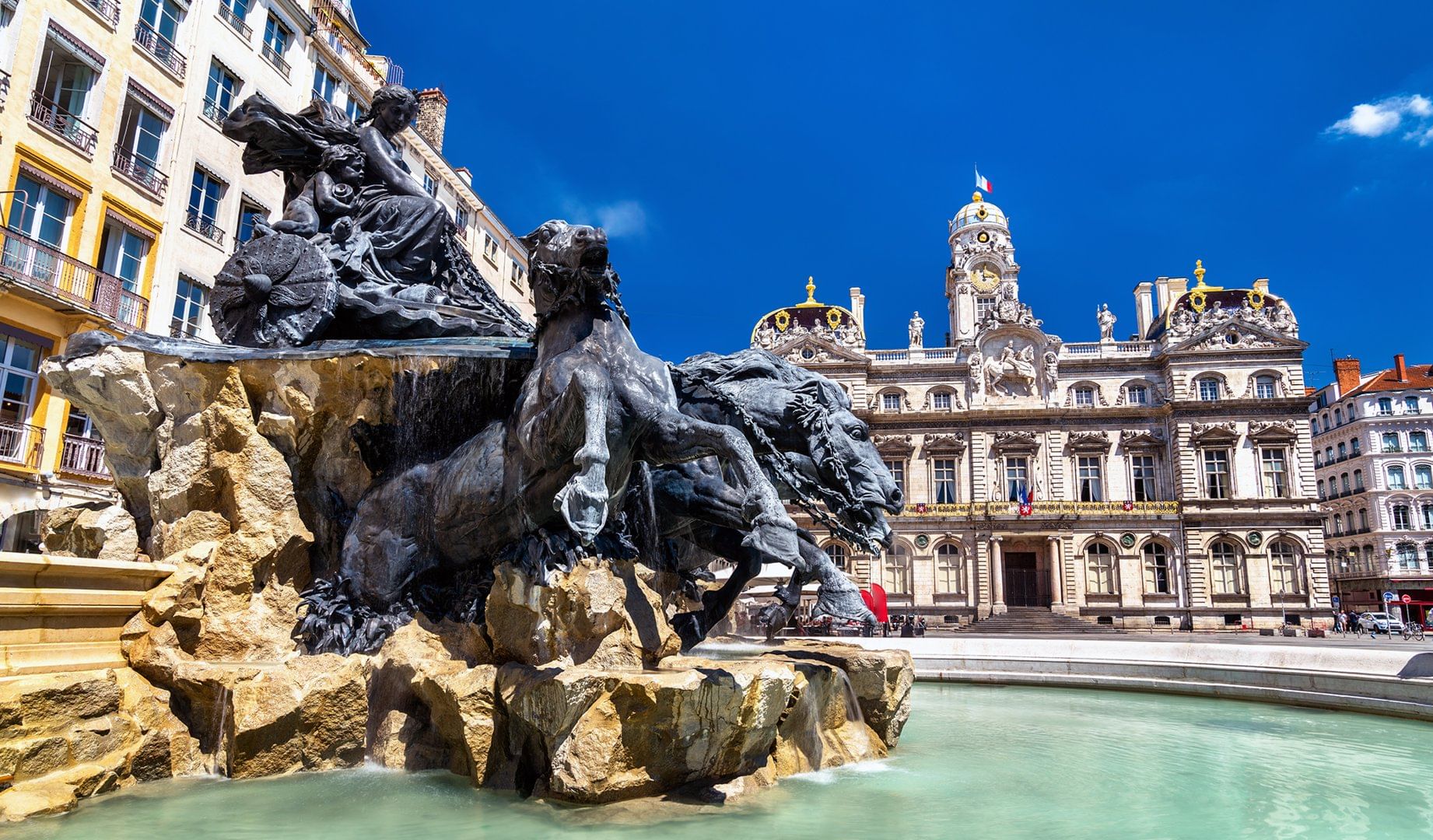 The Fontaine Bartholdi in Lyon’s Place des Terreaux, featuring majestic bronze horses pulling a chariot, with the Hôtel de Ville in the back