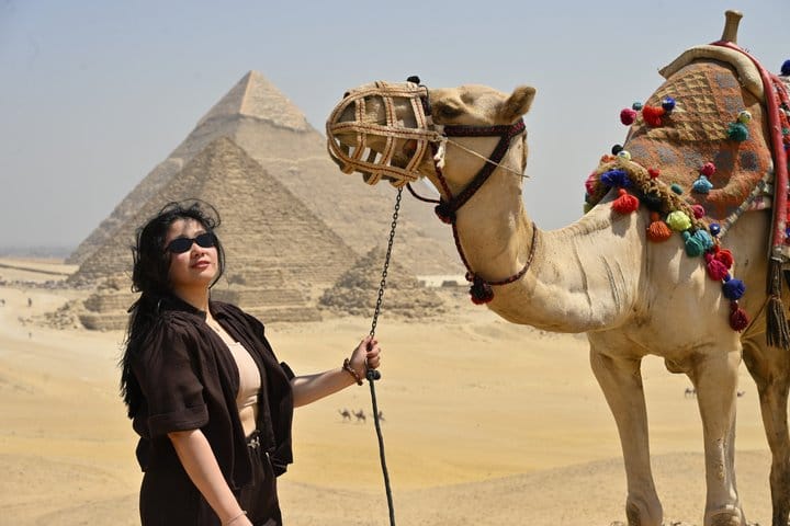 Traveler posing with a decorated camel in front of the Giza pyramids in Egypt