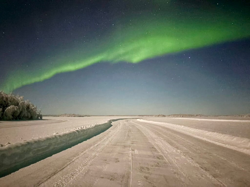 Bright green Northern Lights above a snow-covered frozen lake in Rauduskylä near Levi.