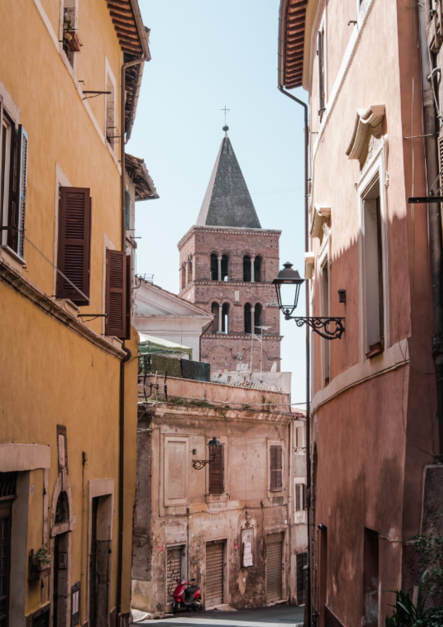 Narrow street in Tivoli’s historic center, with warm-toned buildings, shutters, a lantern, and a bell tower ahead.