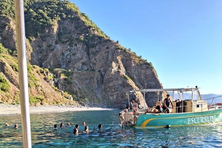 Bateau ancré avec des personnes nageant dans des eaux cristallines le long de la Costa Viola