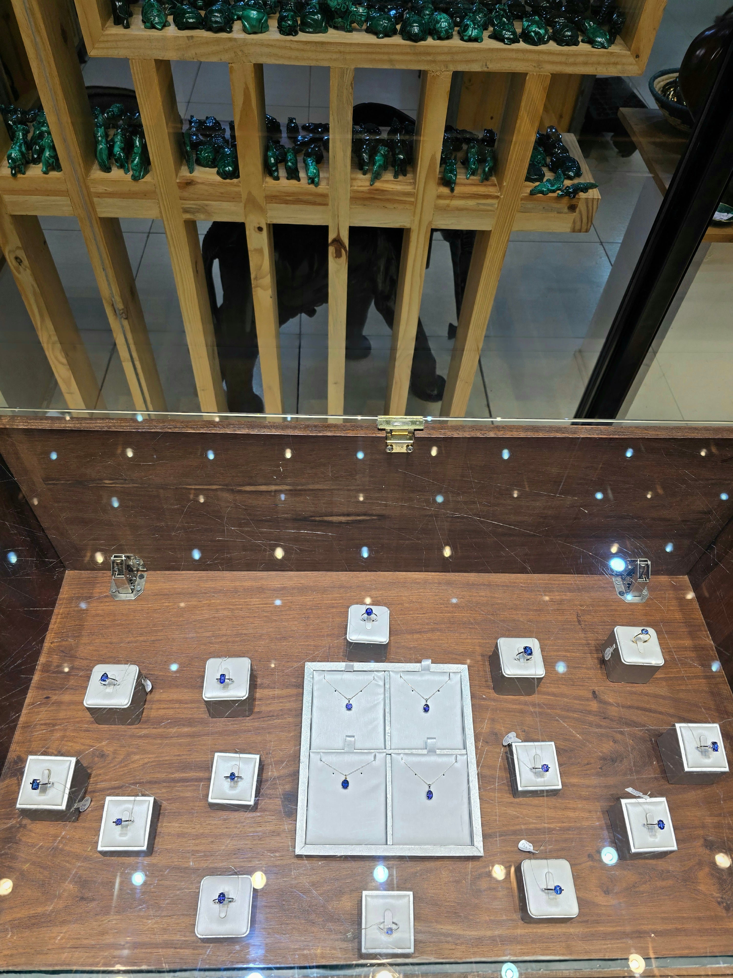 An illuminated wooden display chest showing handcrafted rings, pendants, and gemstone jewelry set on individual stands.