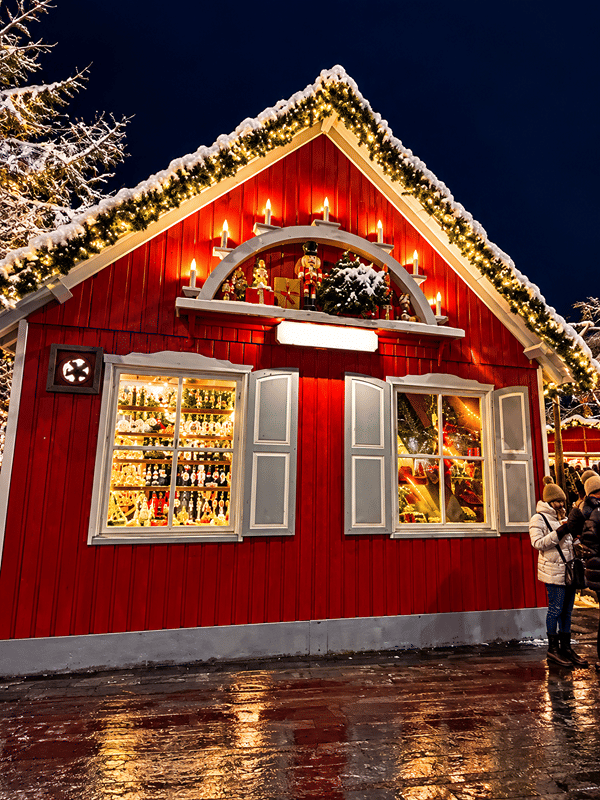 Uma casinha de madeira do mercado de Natal, com enfeites e luzes na neve.