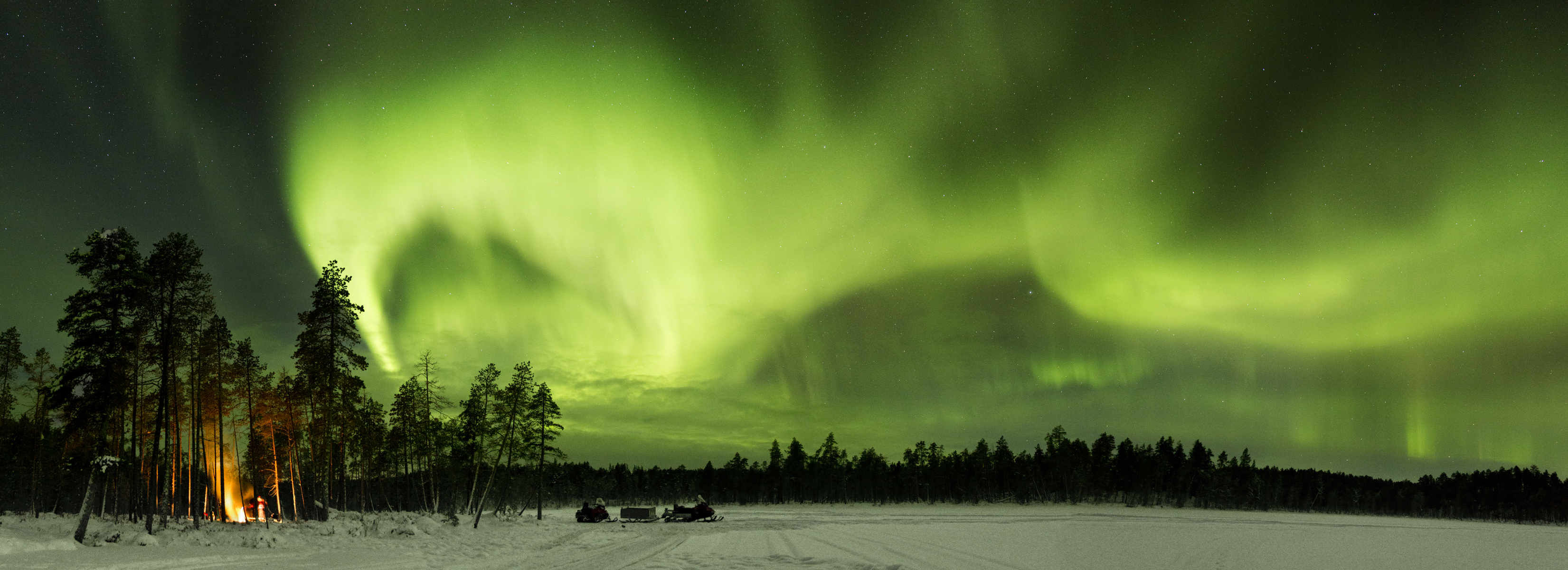 Sleigh pulled by a snowmobile and northern lights on sky