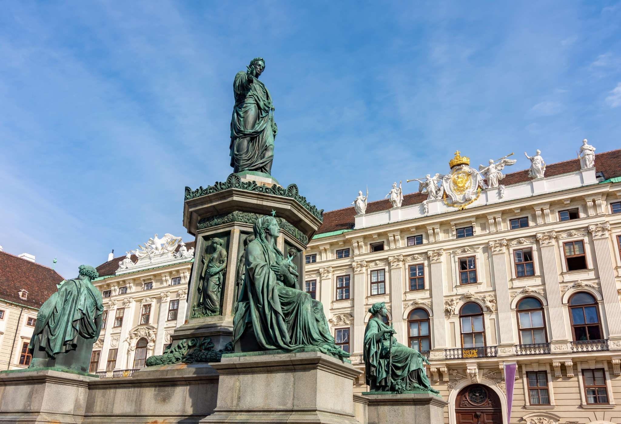 Bronze statue of Emperor Francis I surrounded by figures, with Hofburg Palace in the background under a blue sky