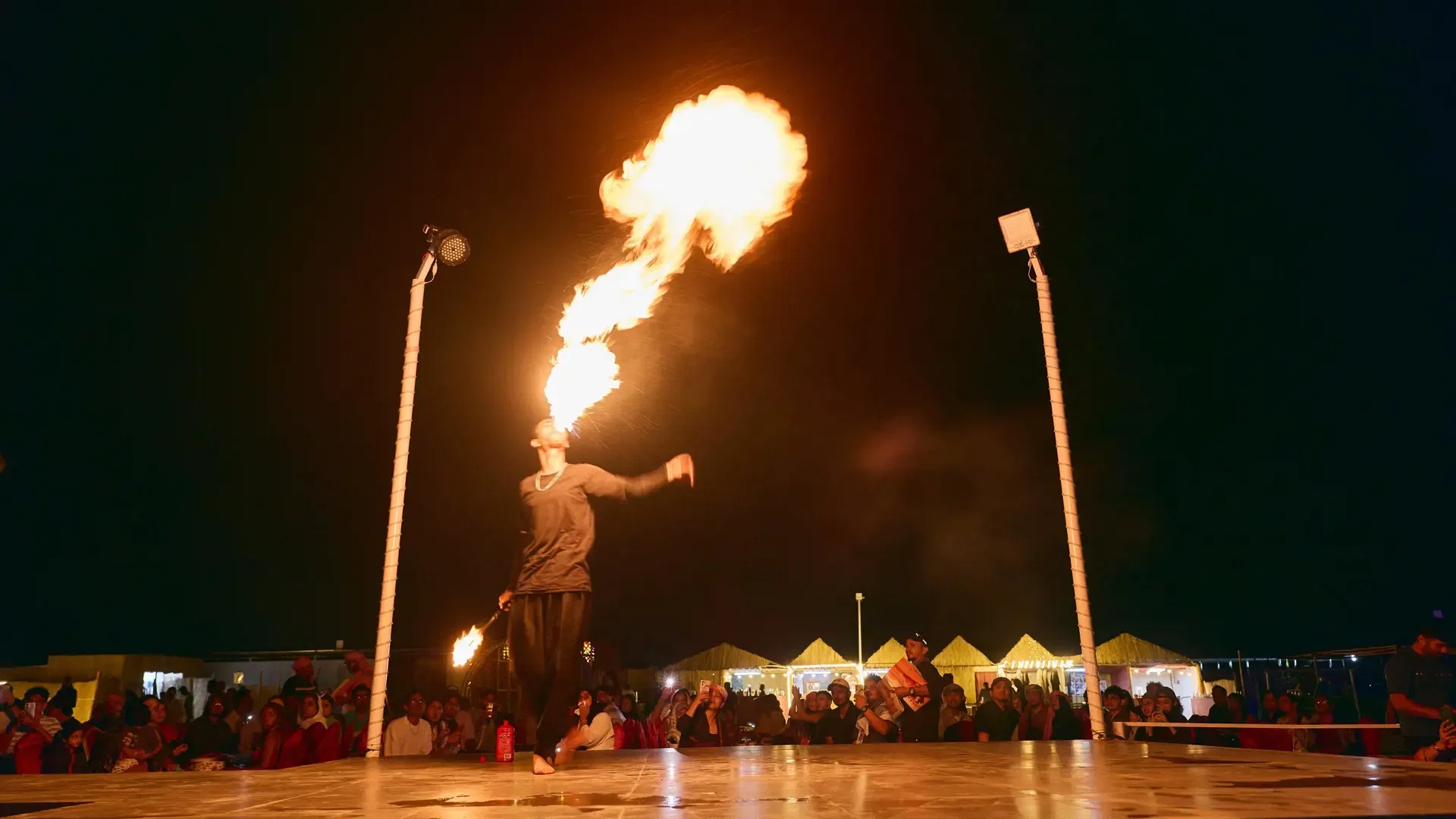 A performer in dark clothing exhales a bright ball of fire on an outdoor stage at Desert Safari + Al Faqaa Camp.