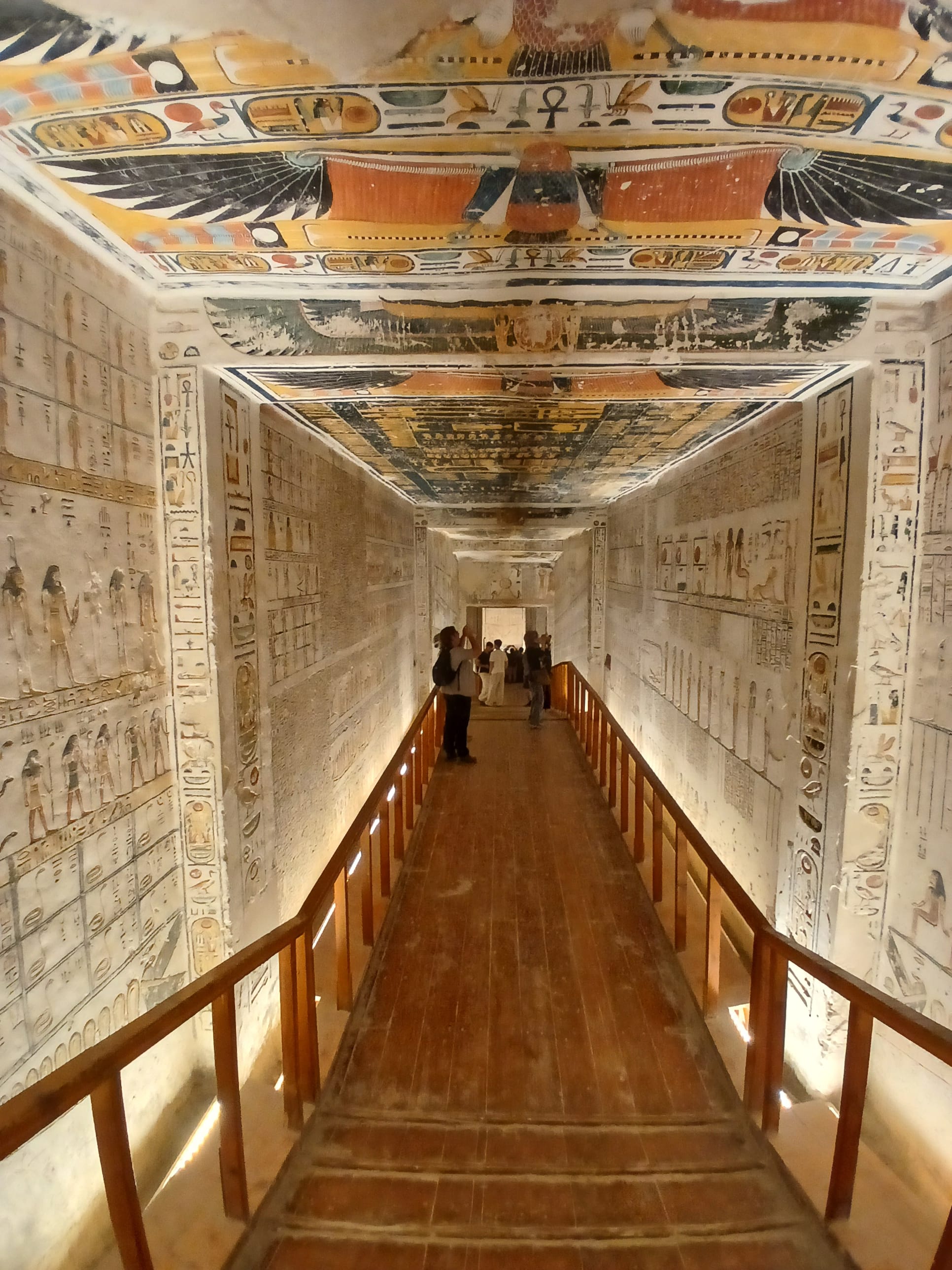 A long, illuminated underground corridor inside the tomb of Merenptah (KV8) in the Valley of the Kings. Visitors are walking along a raised 