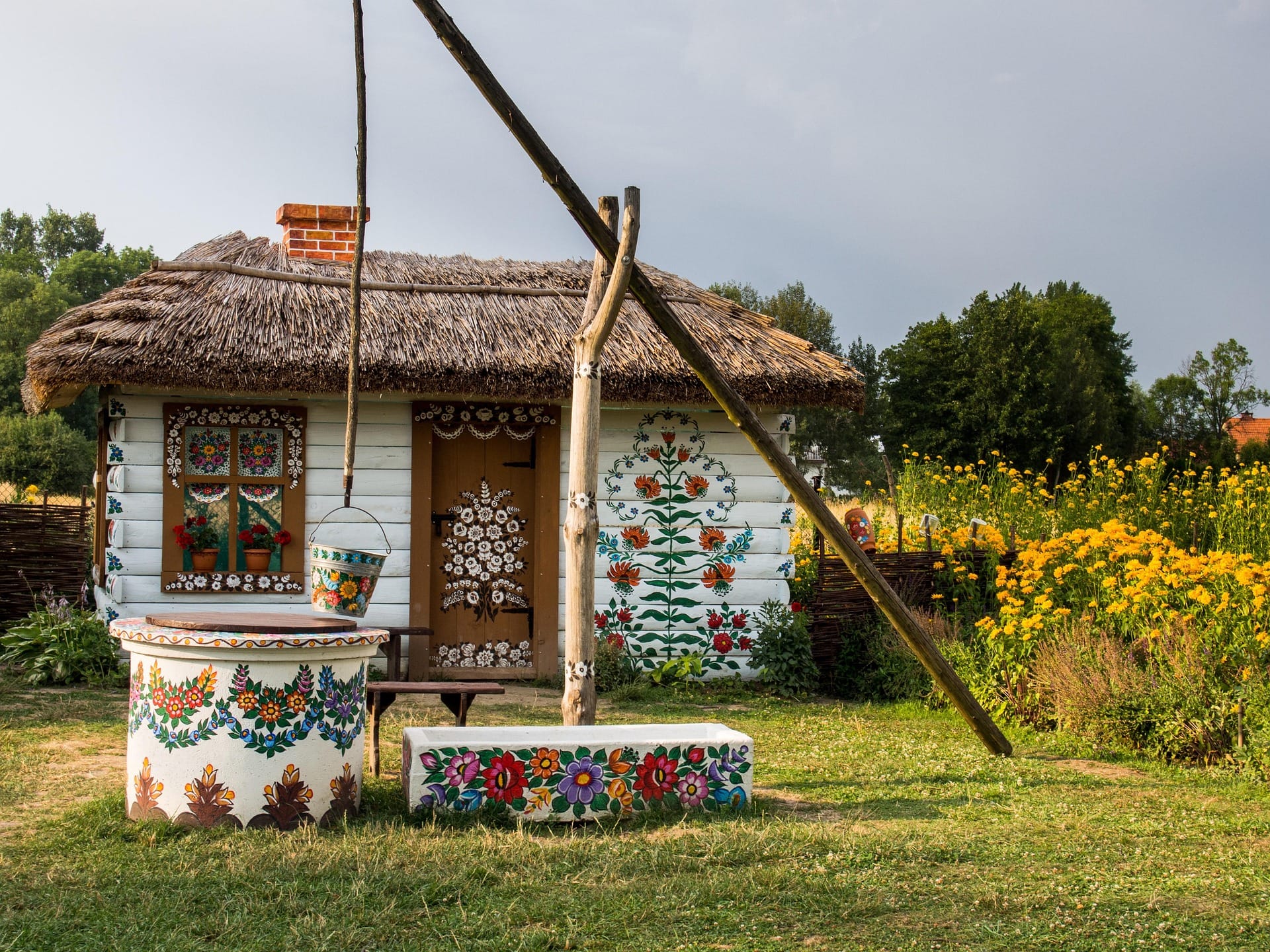 Zalipie painted village cottage summer — folk floral motifs on white house walls with painted well and flowers