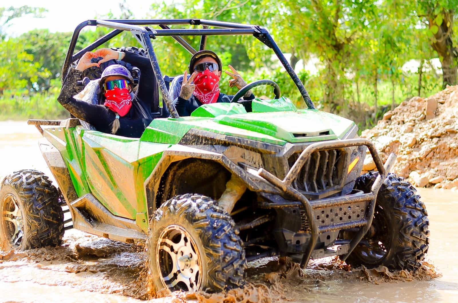 Pareja disfrutando un tour en buggy UTV tipo side-by-side en Punta Cana, cruzando un charco de lodo durante una aventura 4x4 rodeada de natu
