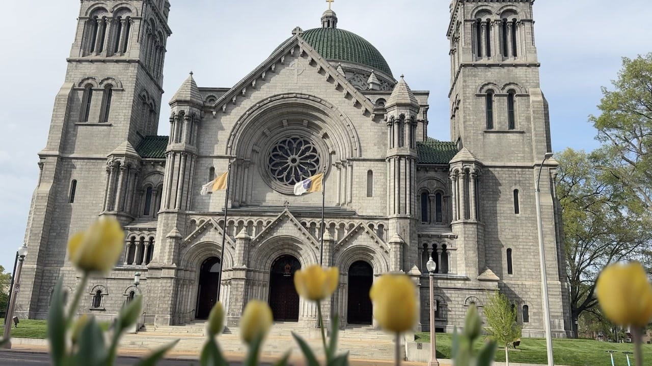 Cathedral Basilica facade with twin towers, green dome, and rose window, yellow tulips blurred in foreground
