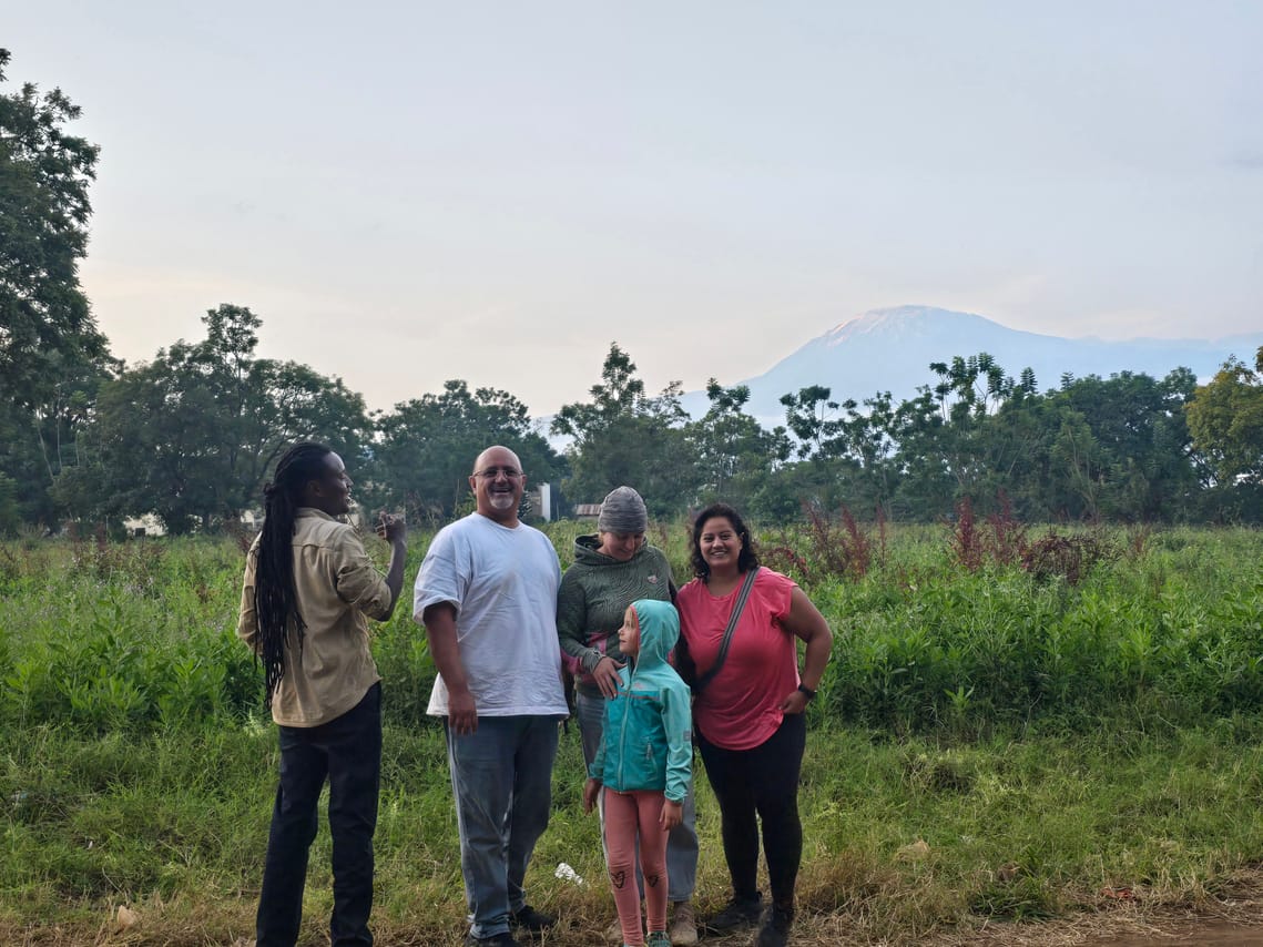 A group of travelers standing outdoors enjoying clear panoramic views of Mount Kilimanjaro peak in the background.