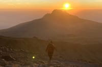 A silhouette of a hiker walking towards a golden sunrise behind a mountain peak on Mount Kilimanjaro.