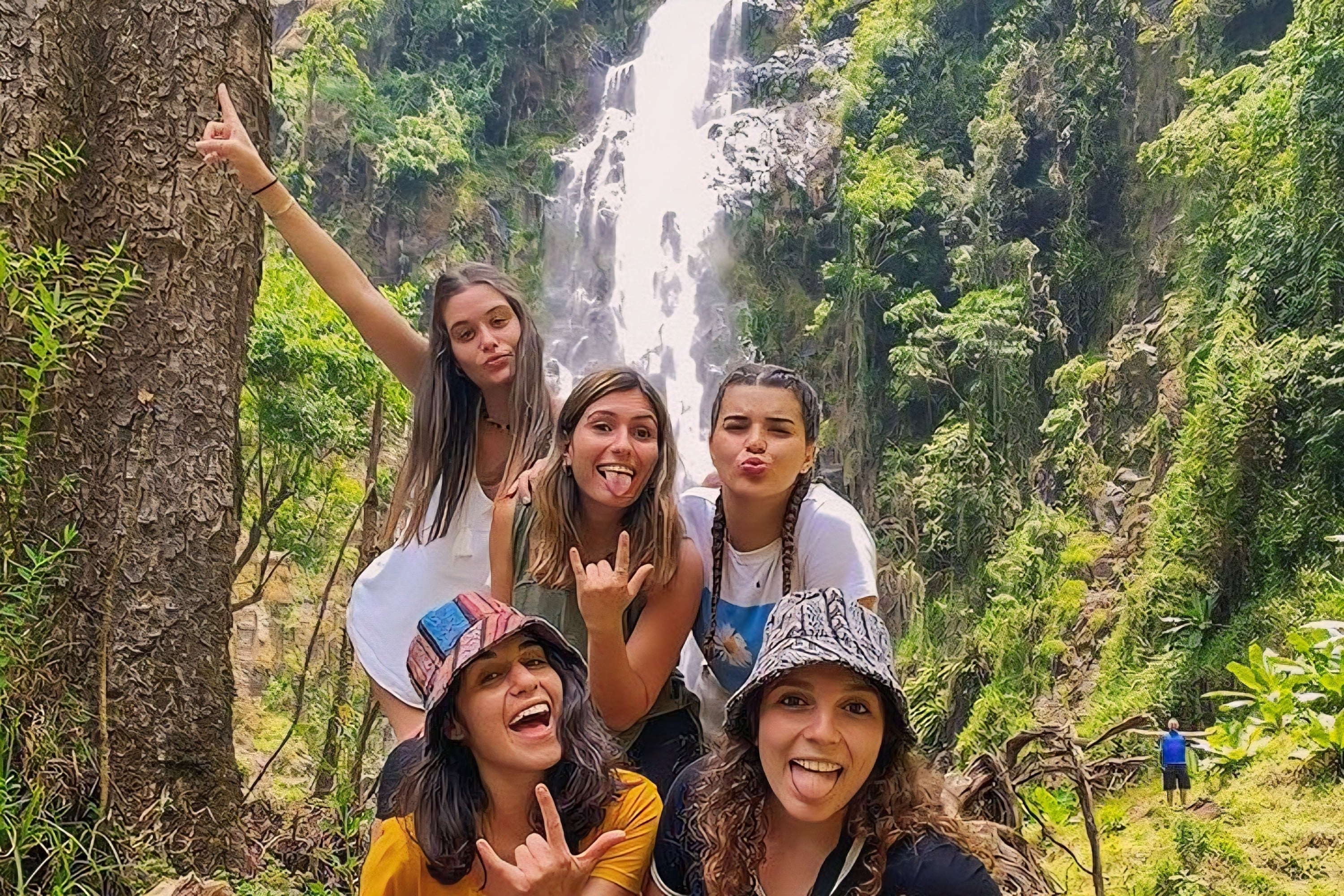 A group of happy travelers posing together in front of Materuni Waterfalls near Mount Kilimanjaro.