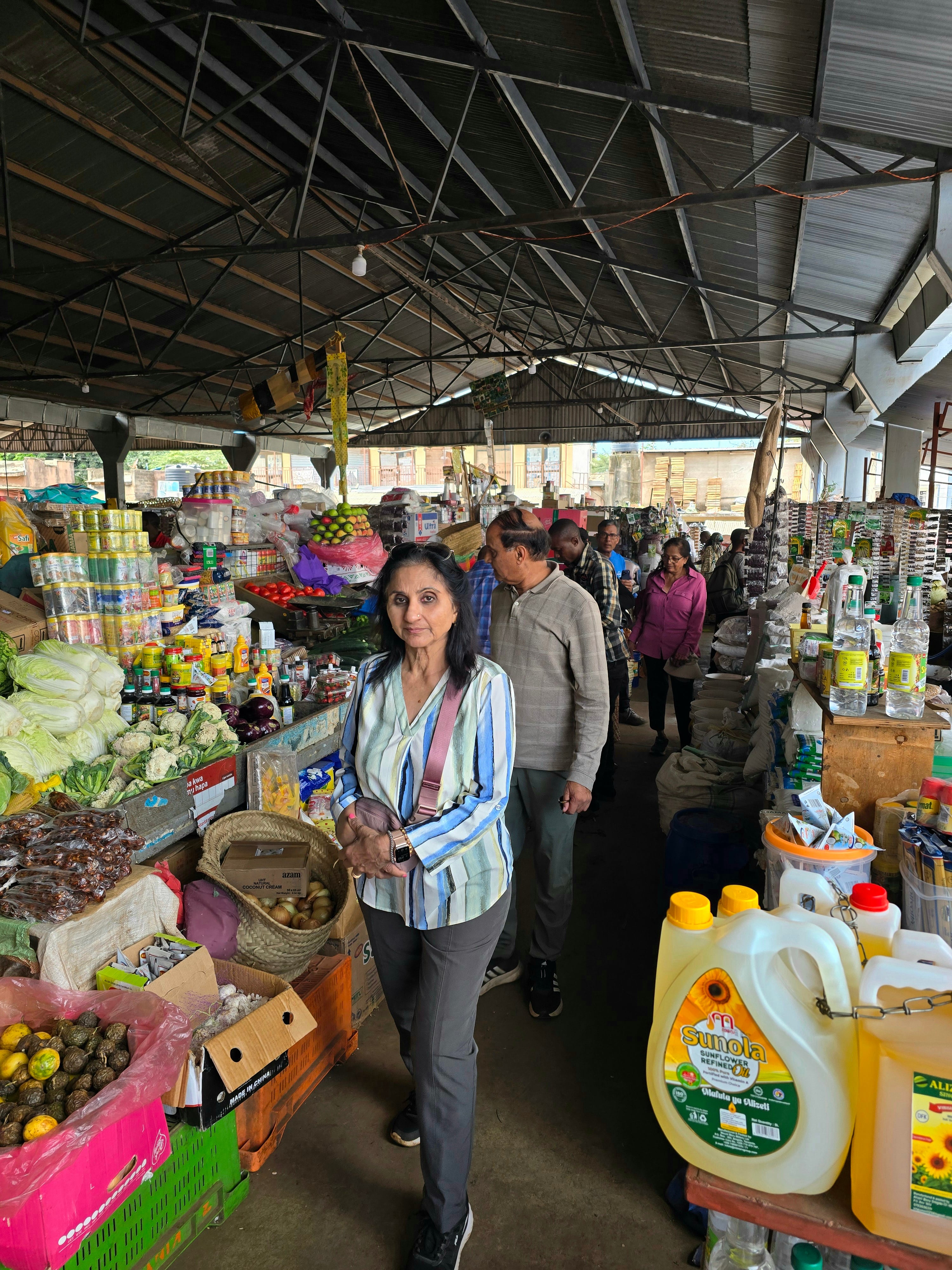 A guest walking through a vibrant open-air market in Moshi surrounded by fresh local produce stalls.