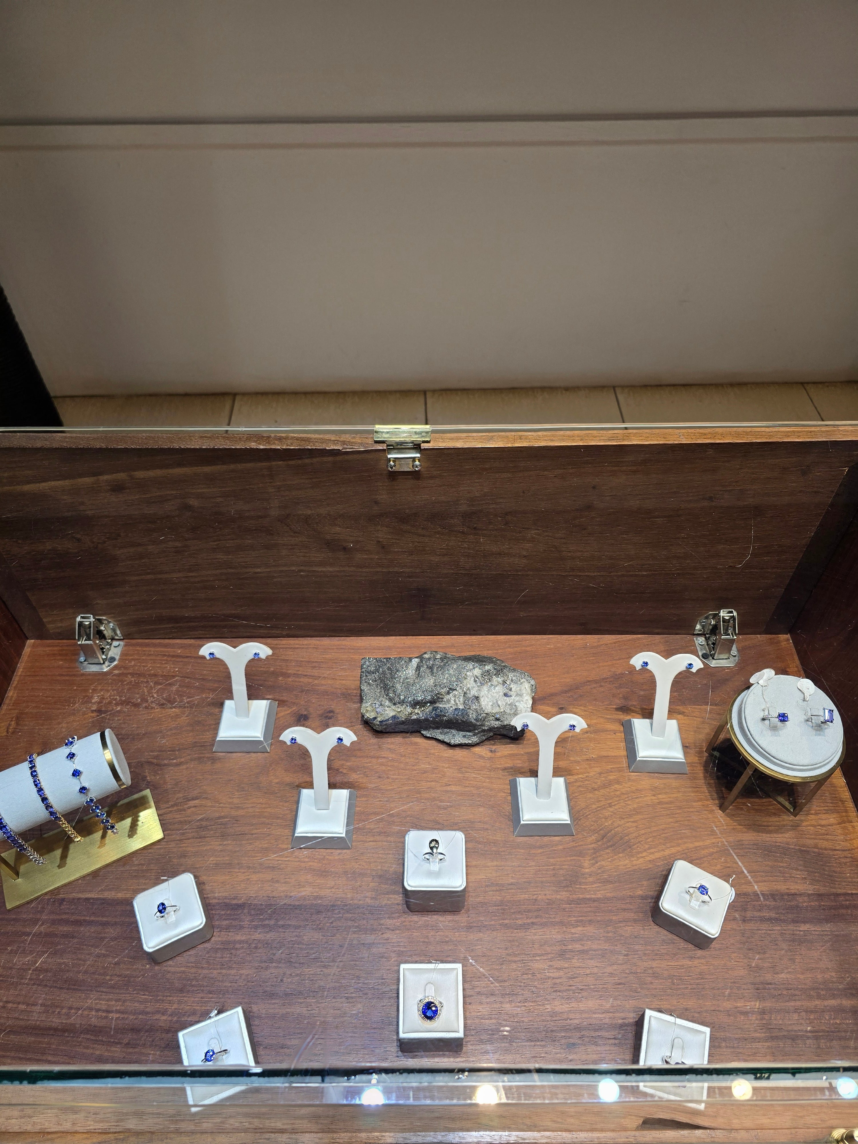 A wooden display cabinet showcasing fine handcrafted Tanzanian jewelry, earrings, and polished gemstone ornaments.