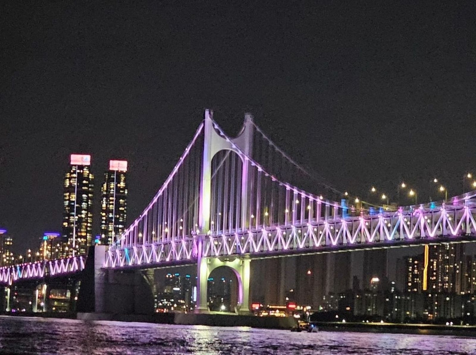 Gwangandaegyo Bridge lit up at night in Busan with reflections on the water.