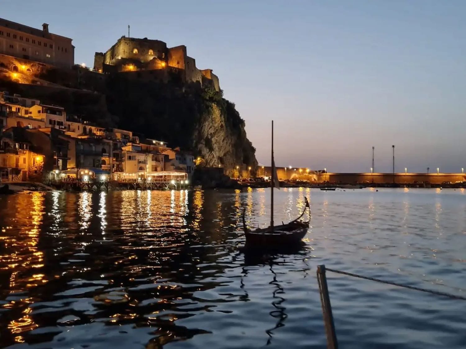 Barca che galleggia su acque calme con il tramonto sulla Costa Viola