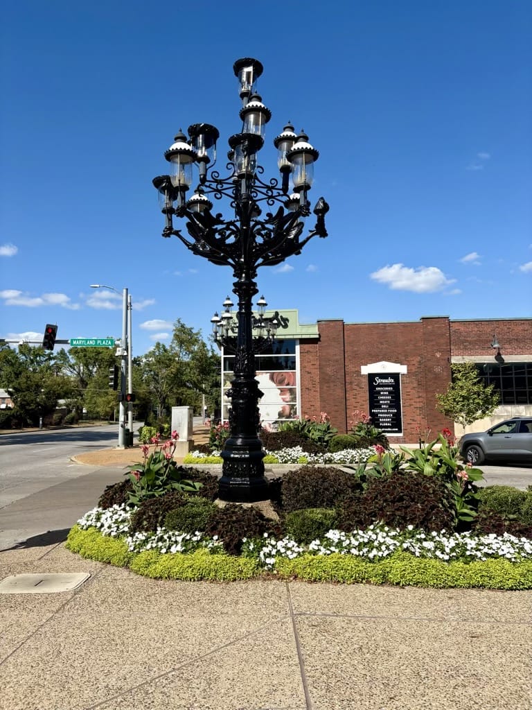 Ornate cast-iron candelabra streetlamp with multiple lights, in the center of a flower bed on Maryland Plaza