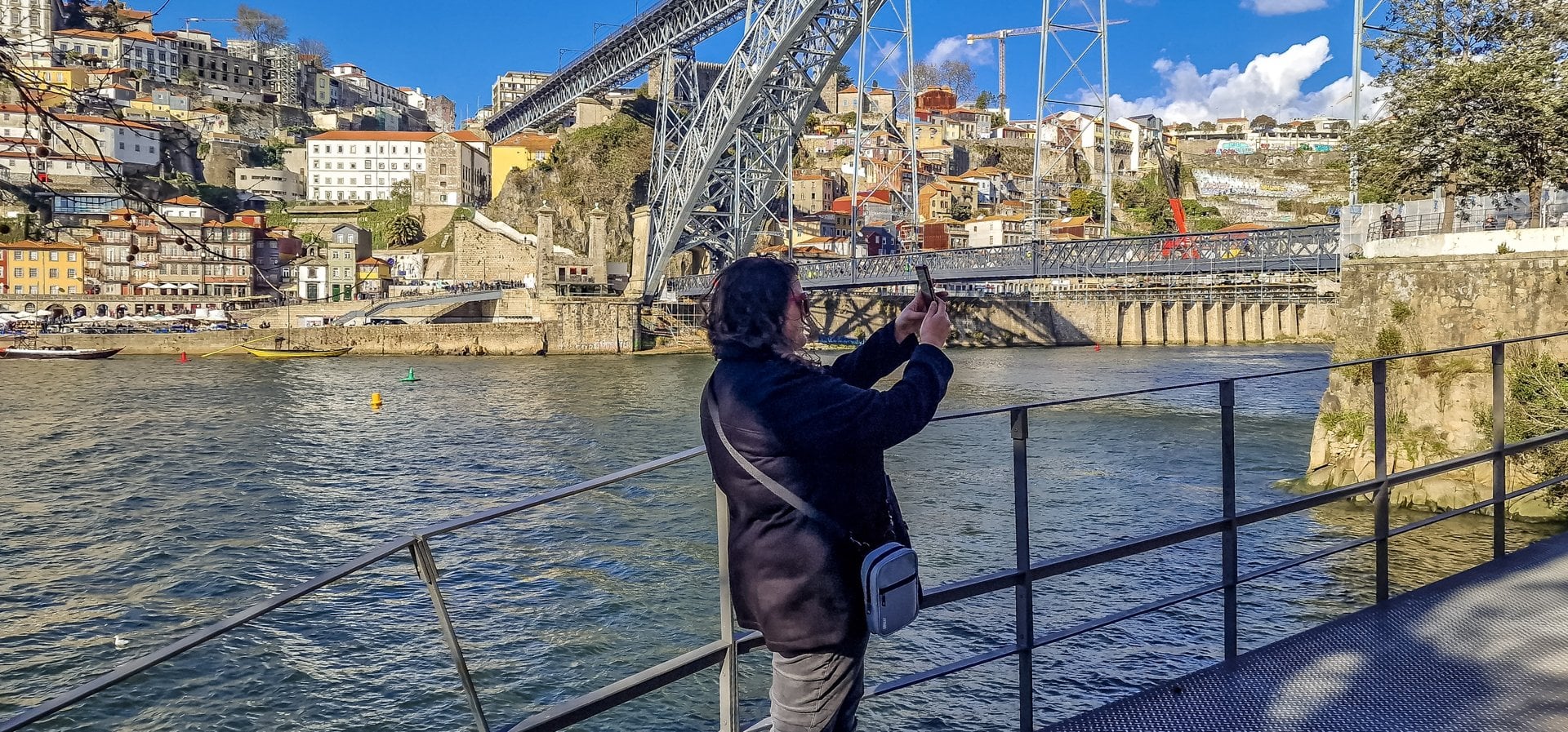 A visitor photographing the Dom Luís I Bridge and the Ribeira in Porto from the Douro river
