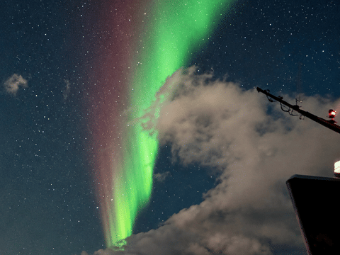 Green Northern Lights glowing through the clouds over the ocean near Reykjavík, Iceland.