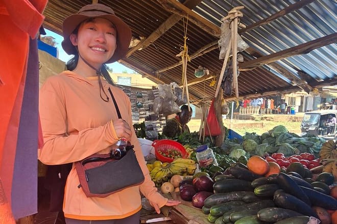 A traveler posing at a bustling open-air market stall stocked with various fresh fruits and vegetables.