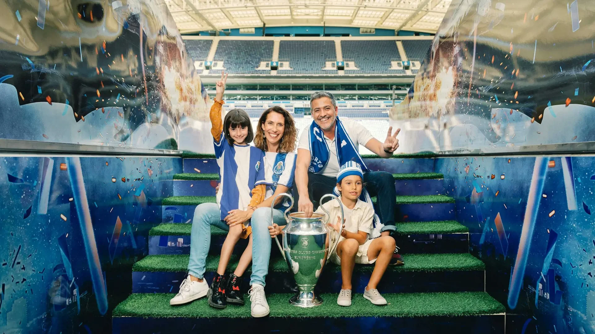 A smiling family of four in blue-and-white striped shirts poses on stadium stairs next to a large trophy at FC Porto Museum & Dragão Stadium ticket.