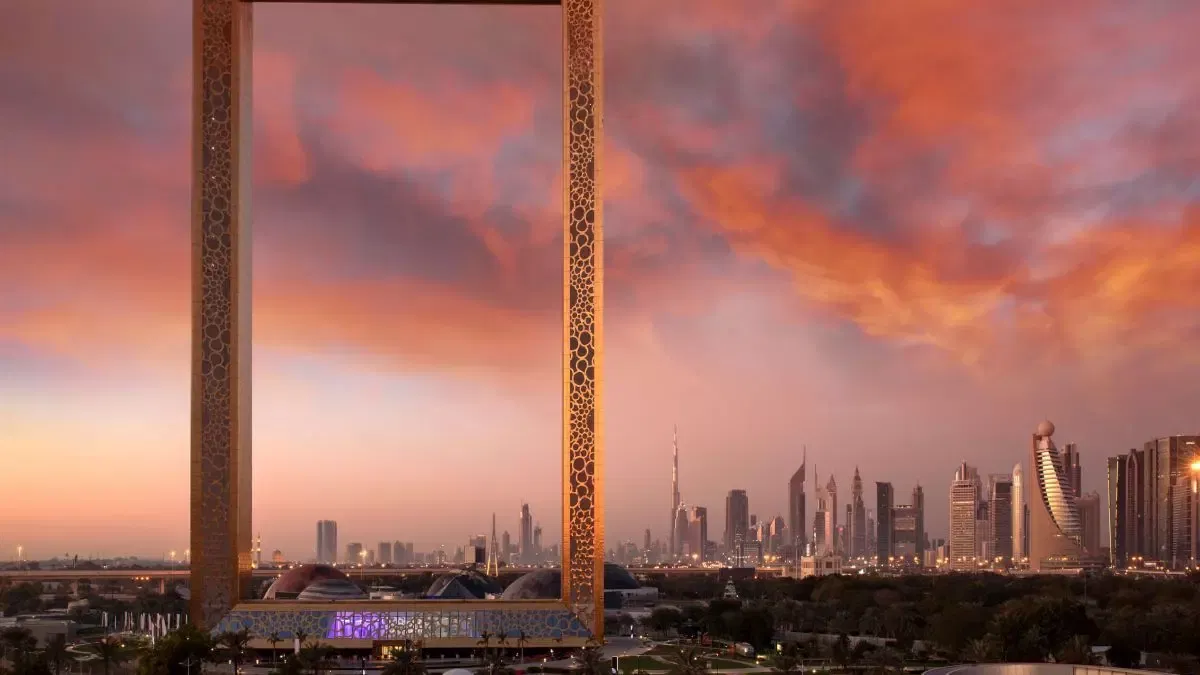 The golden Dubai Frame at sunset with open sky and cloud framed in its opening, the city skyline visible beyond its right column, at Dubai Frame