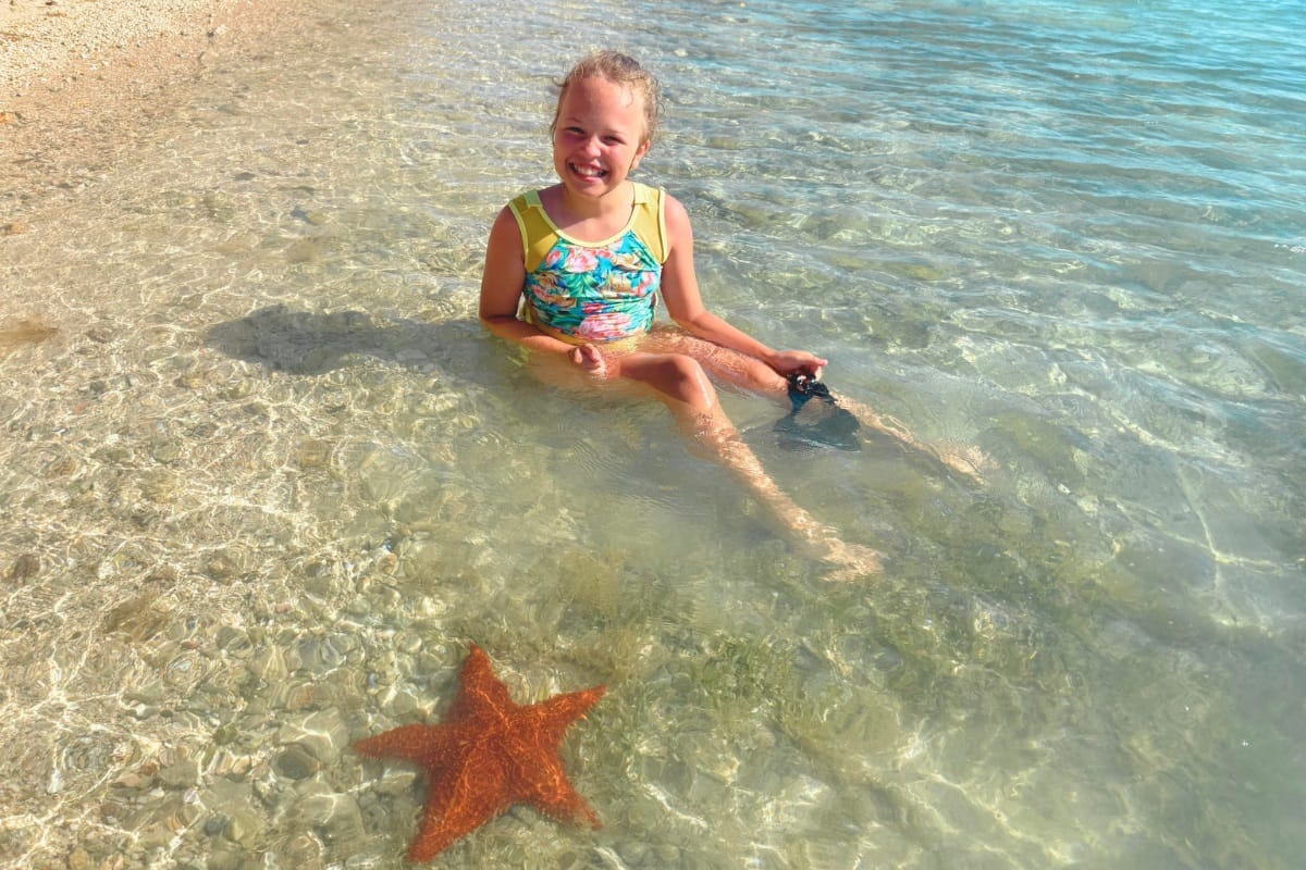 smiling child facing a starfish while snorkeling at the beach of fuik Bay