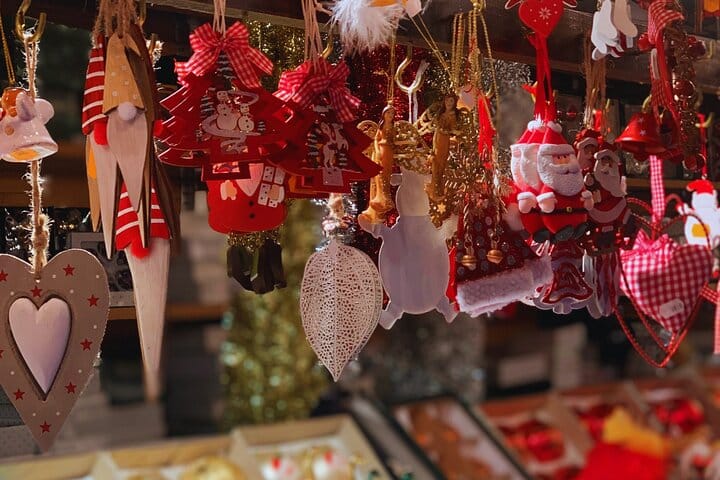 Divers ornements et décorations de Noël (cœurs, Pères Noël, gnomes, étoiles) rouges et blanches suspendus dans un étal de marché.
