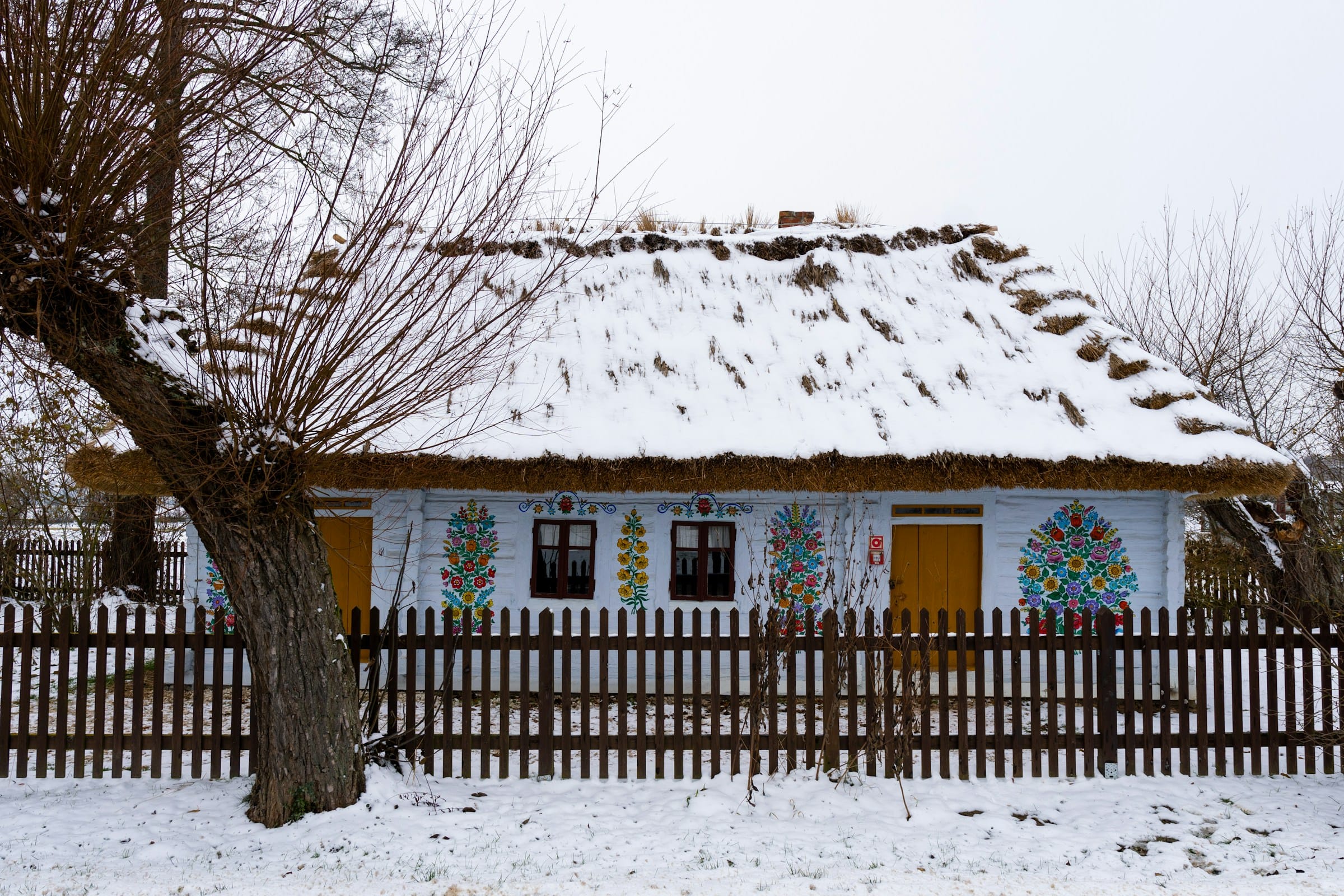 Zalipie painted village winter — traditional cottage with floral folk art snow on thatched roof Poland