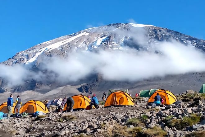 Bright orange tents at a high-altitude base camp with the snow-capped peak of Mount Kilimanjaro in the background.