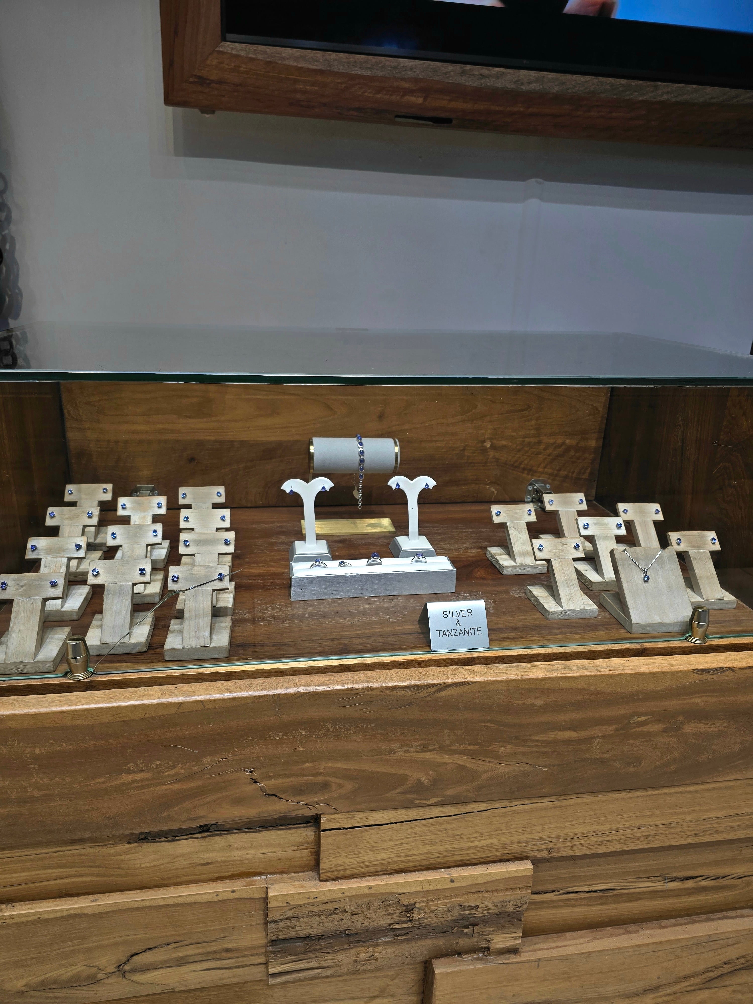 A wooden display counter showcasing a collection of custom handmade jewelry, including rings and bracelets set on white stands.