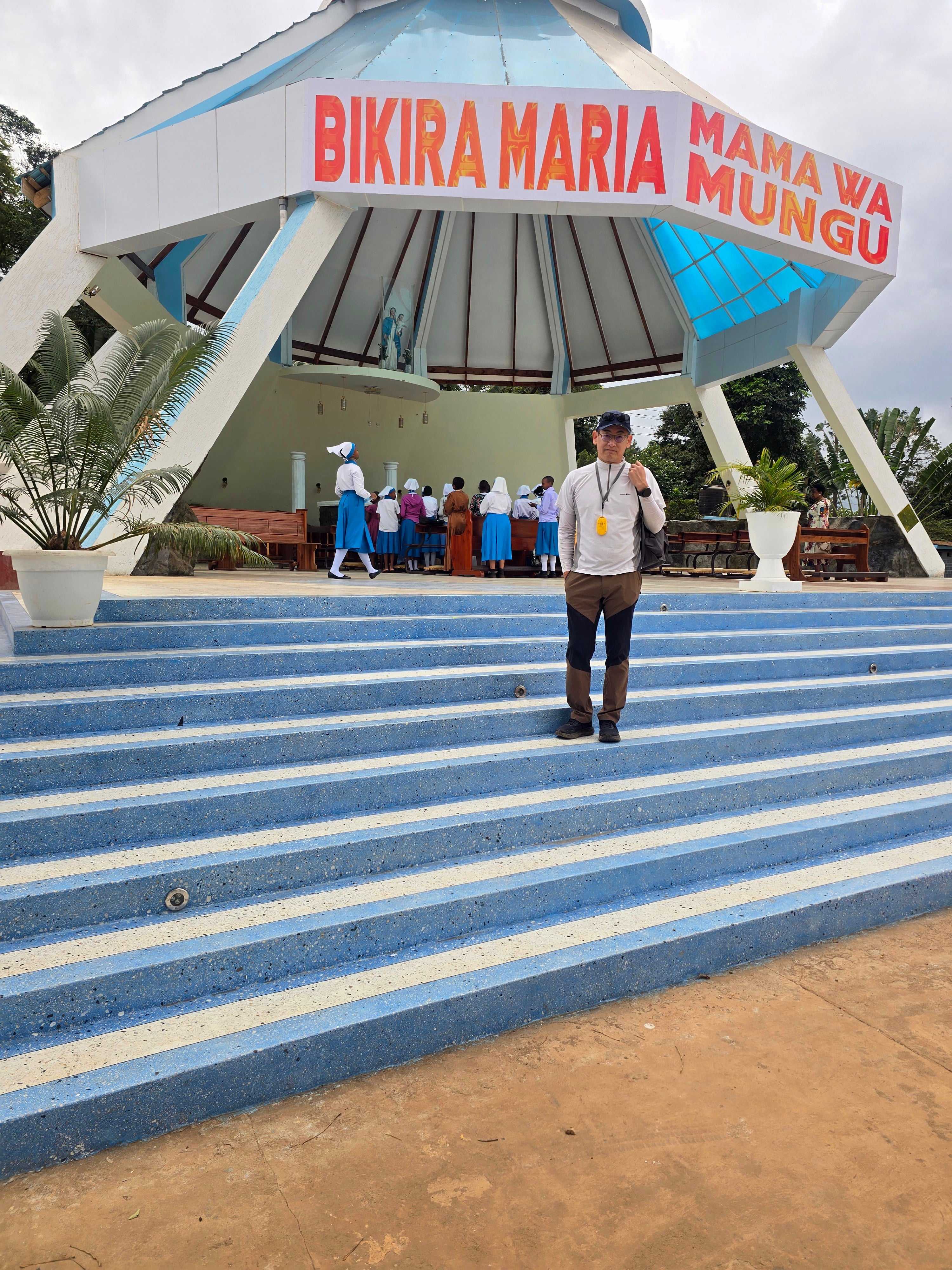 A guide standing on wide outdoor blue-tiled steps leading up to an open pavilion entrance at Christ the King Cathedral.