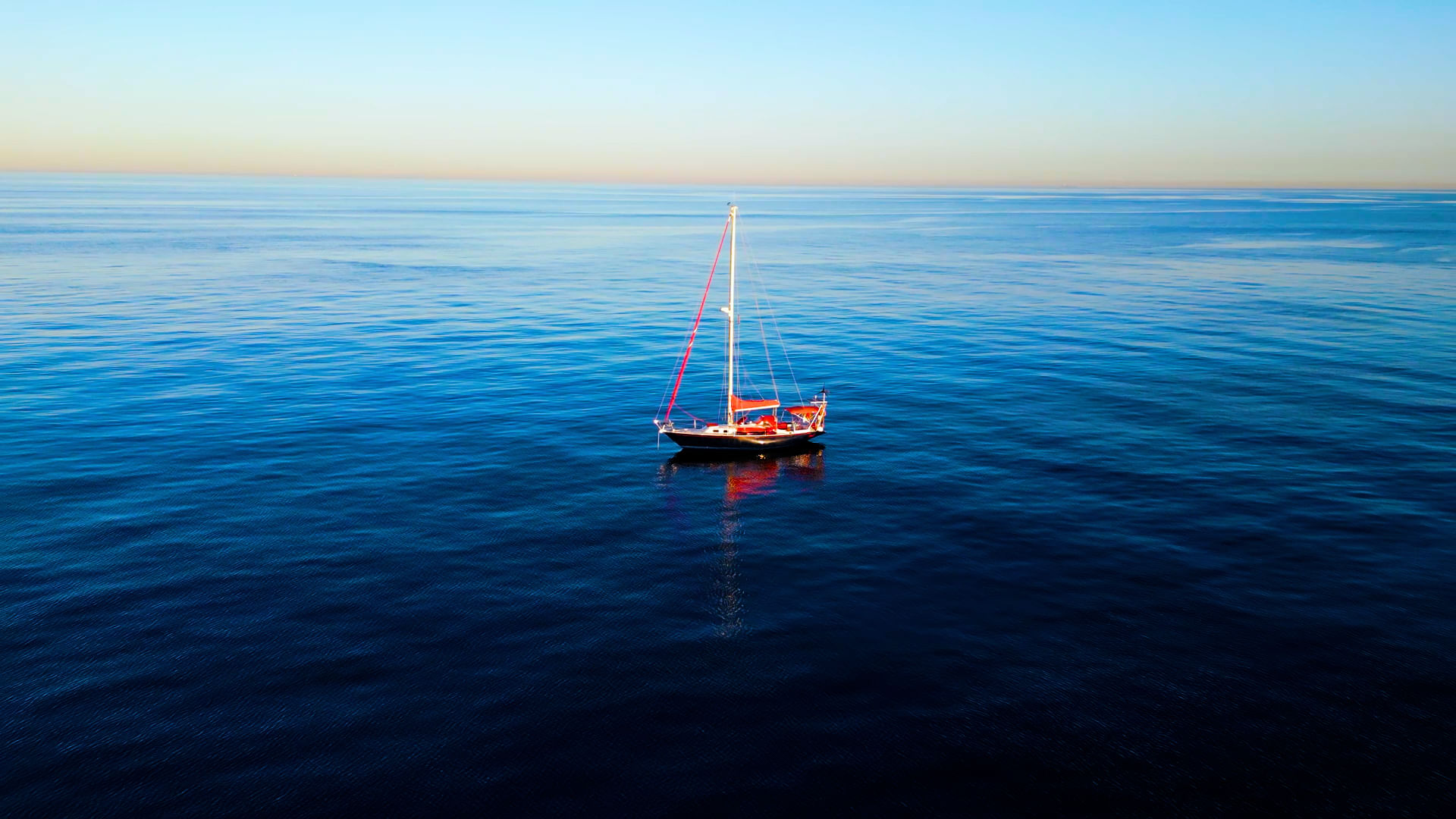 El velero rojo Assol flotando en medio del mar Mediterráneo, con un horizonte lejano y un cielo despejado que se funde con el agua, creando 