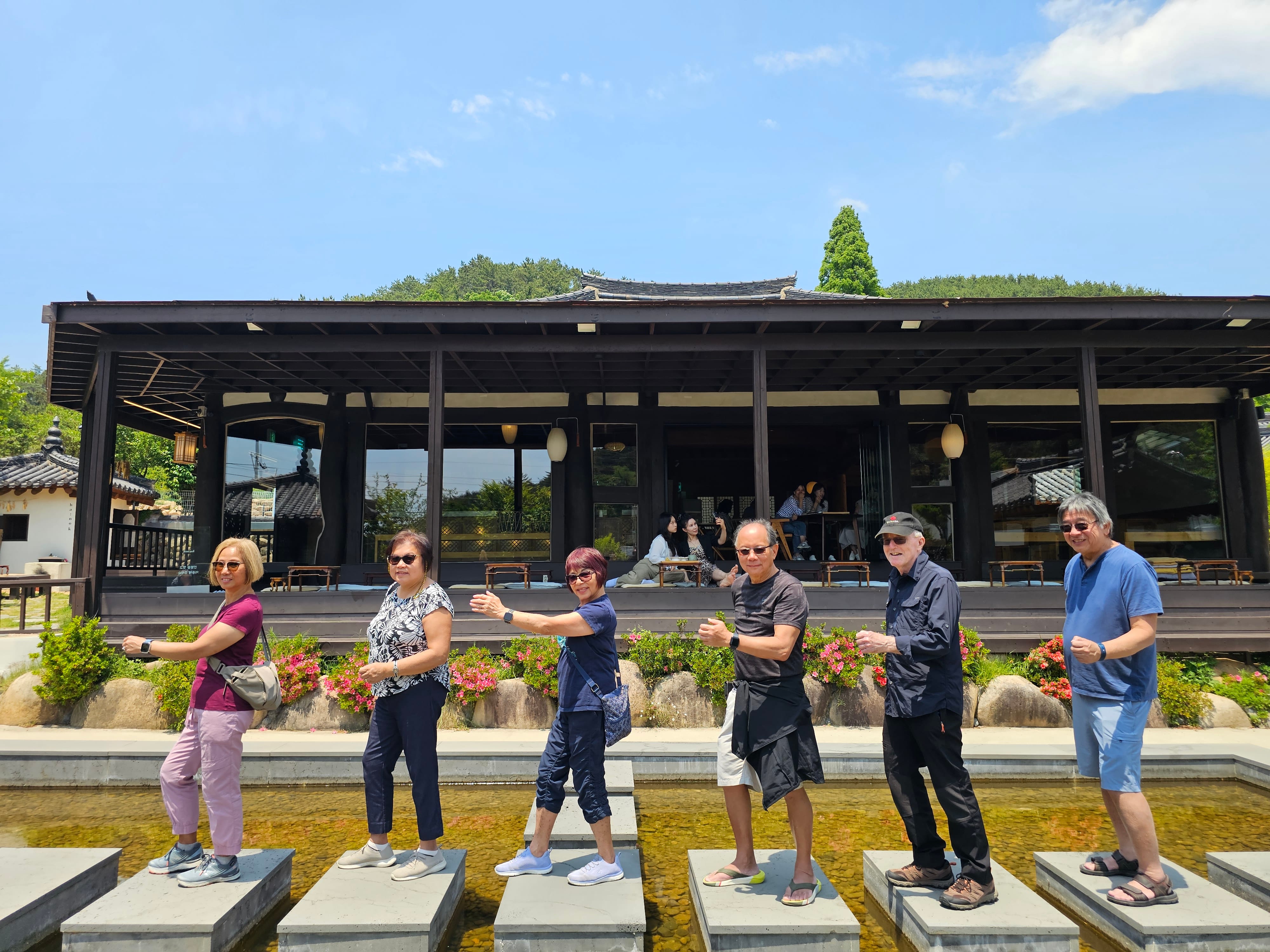 A group poses playfully in a row on stepping stones outside Ha:nok Cafe, a traditional hanok-style cafe.