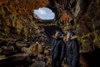 People standing inside a lava cave looking toward a natural opening above