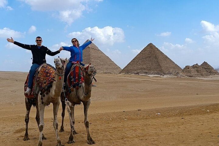 Two tourists riding camels with the Pyramids of Giza in the distance.