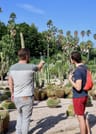 The guide is standing in front of a cactus garden and explaining the plants to the guest.