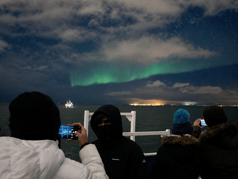 Guests enjoying the Northern Lights from the deck of a boat during an evening cruise in Iceland.