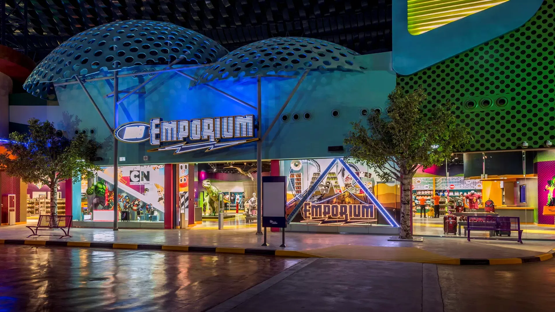 A brightly lit store facade features blue and yellow signage with round structural covers at IMG Worlds of Adventure Theme Park.