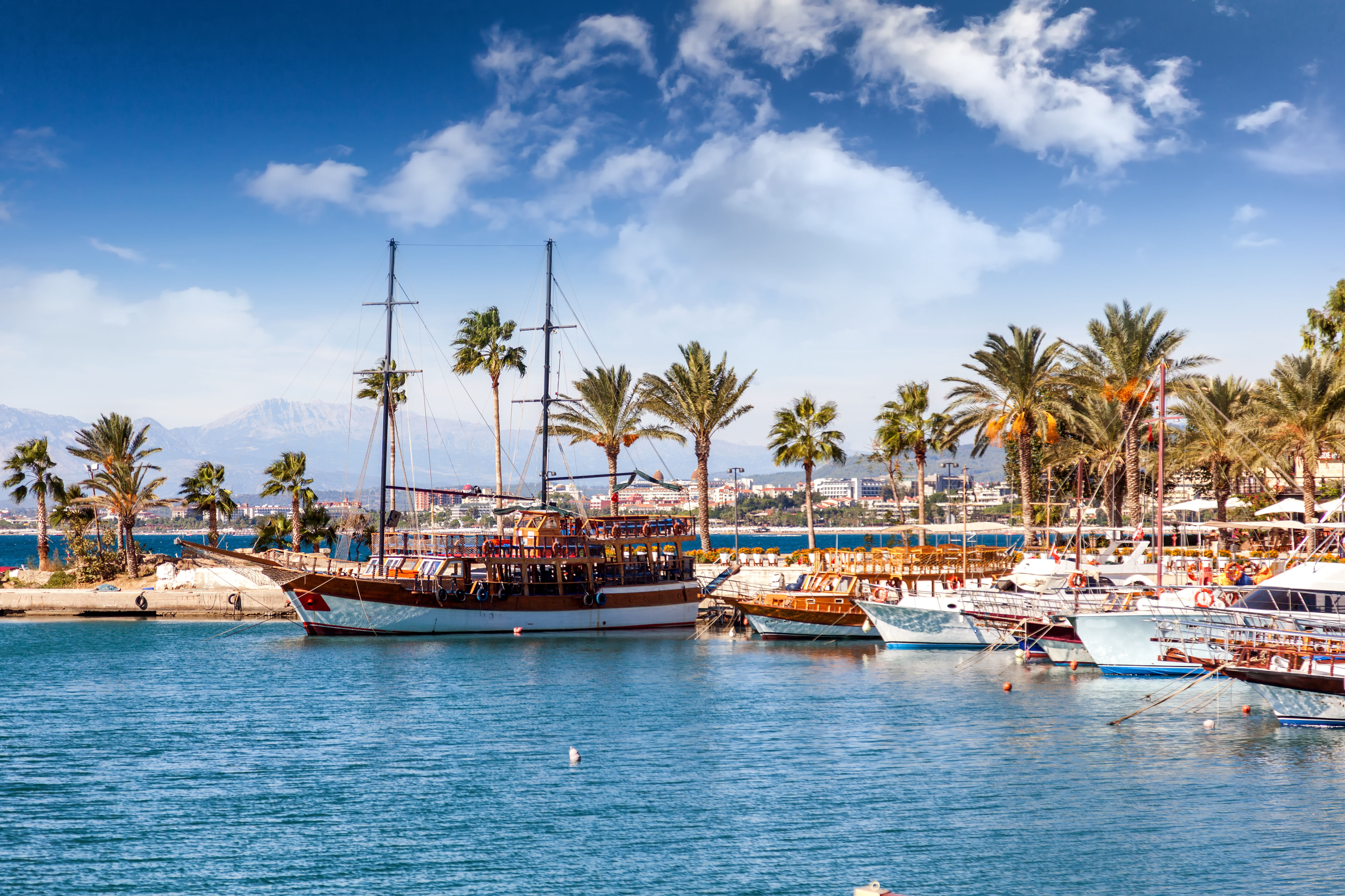 “Sightseeing boats docked at the port of Side, Turkey, with clear blue waters and Mediterranean-style buildings along the shoreline.”