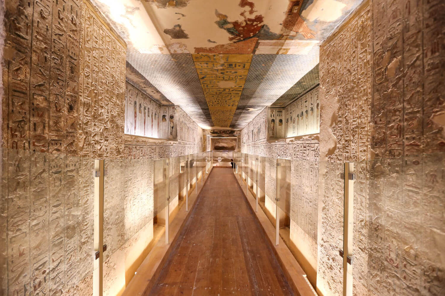A long corridor inside an ancient Egyptian tomb in the Valley of the Kings, with detailed hieroglyphics carved on the walls and colorful pai