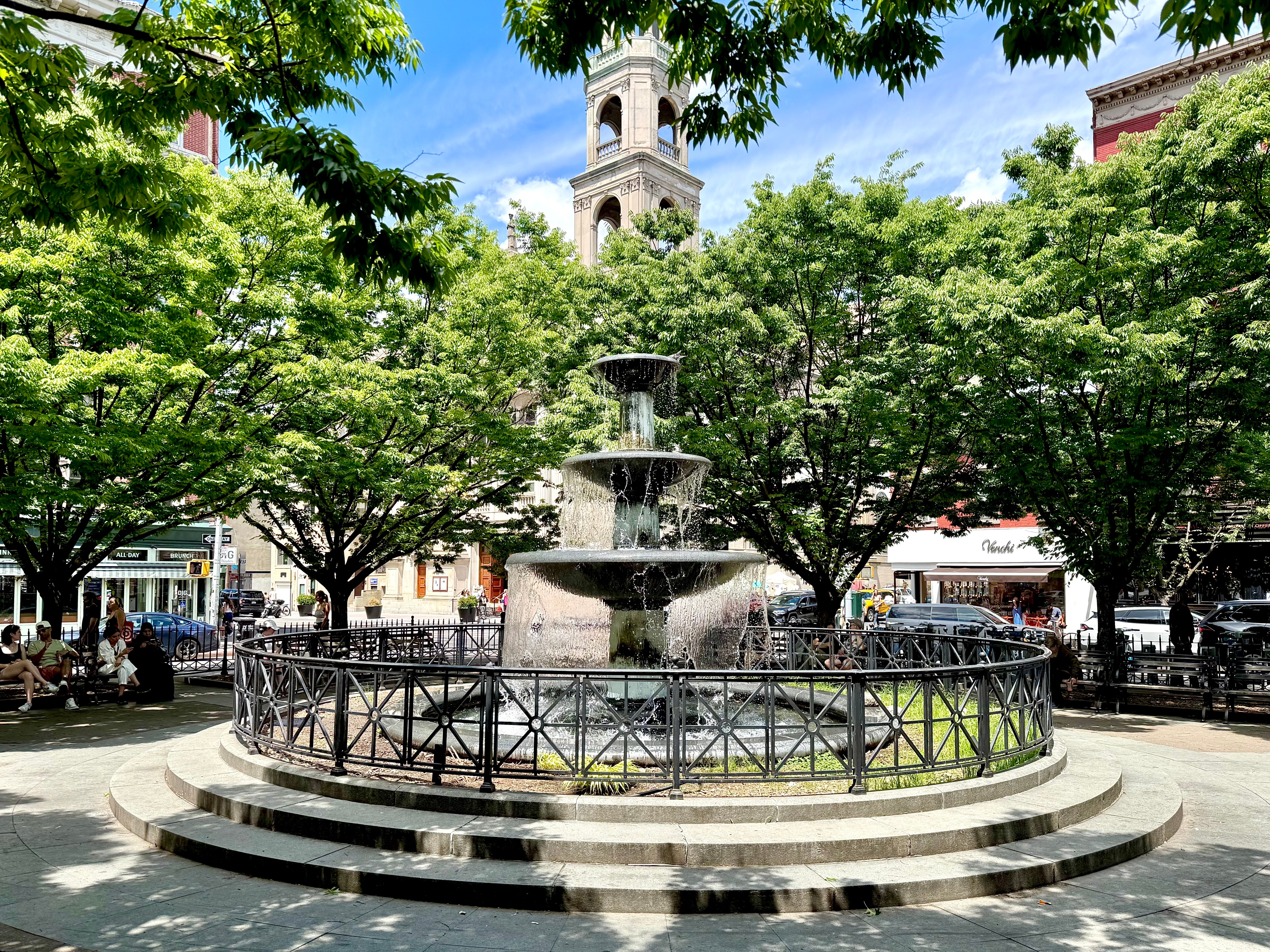A fountain surrounded by trees and a circular railing in Father Demo Square.