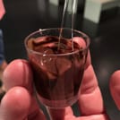 A glass with fresh, melted chocolate is held in the hand by a guest